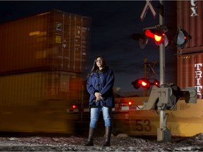 Maple Crest resident Cristina Jarvis poses for a photo as a train passes in the background, in Edmonton Friday Jan. 15, 2021. Jarvis is concerned that a train crossing at the one entrance and exit to the neighbourhood can block emergency crews. Photo by David Bloom