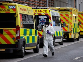 A medical delivery driver wearing PPE runs along a line of parked ambulances outside the Royal London hospital in London on January 19, 2021.