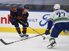 Edmonton Oilers captain Connor McDavid (97) looks to get past Vancouver Canucks' Travis Hamonic (27) in Edmonton on Wednesday, Jan. 13, 2021.