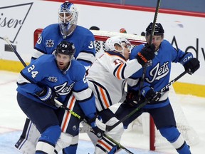 Edmonton Oilers winger Jesse Puljujarvi (centre) is given a rough ride by Winnipeg Jets defenceman Derek Forbort (left) and Neal Pionk (right) in front of goaltender Laurent Brossoit in Winnipeg on Sun., Jan. 24, 2021.