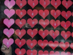 Sara Edwards adds 54 more paper hearts to a memorial at All Saints' Anglican Cathedral, 10035 103 St., in Edmonton Friday Jan. 29, 2021. Hundreds of paper hearts, one for every Albertan who has died from COVID-19, adorn the front of the church.