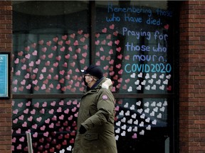A pedestrian wearing a mask to protect against COVID-19 walks past hundreds of paper hearts posted on the windows of All Saints' Anglican Cathedral, 10035 103 St., in memory of people lost to COVID-19 on Thursday, Jan. 21, 2021. The paper hearts stretch around the front of the building.