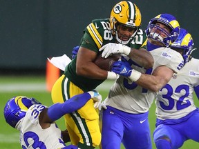Green Bay Packers running back AJ Dillon (28) runs with the ball while Los Angeles Rams safety Nick Scott (33) and linebacker Troy Reeder (51) attempt to tackle him on Jan. 16, 2021, at Lambeau Field.