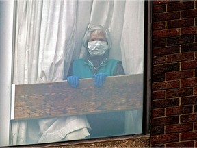 A woman looks out the window of her apartment at a seniors residence in downtown Edmonton during the COVID-19 pandemic on March 29, 2020.