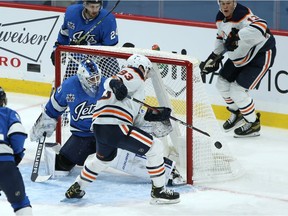 Edmonton Oilers forward Ryan Nugent-Hopkins is unable to control a bouncing puck in front of Winnipeg Jets goaltender Laurent Brossoit in Winnipeg on Jan. 24, 2021.