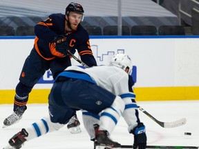 Edmonton Oilers’ Connor McDavid (97) passes past Winnipeg Jets’ Neal Pionk (4) during first period NHL action at Rogers Place in Edmonton, on Monday, Feb. 15, 2021.