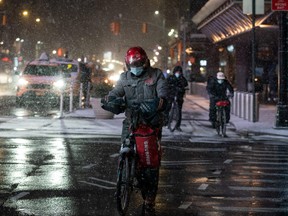 A delivery person wearing a protective mask rides his bike as snow begins to fall in Times Square during a snow storm, during the pandemic in the Manhattan borough of New York City, U.S., Jan. 31, 2021.