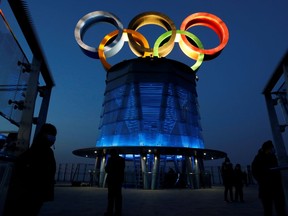 People wearing face masks following the coronavirus disease (COVID-19) outbreak are seen near the lit-up Olympic rings at top of the Olympic Tower, a year ahead of the opening of the 2022 Winter Olympic Games, in Beijing, China February 4, 2021.