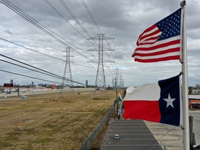 The U.S. and Texas flags fly in front of high voltage transmission towers on Feb. 21, 2021, in Houston. Millions lost power when a winter storm hit the state and knocked out coal, natural gas and nuclear plants that were unprepared for the freezing temperatures brought on by the storm. Wind turbines that provide an estimated 24 per cent of energy to the state became inoperable when they froze.