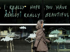 A pedestrian, wearing a mask to protect against COVID-19, makes their way past a message on the front window of Tix On the Square box office and store, 9930 102 Ave., in Edmonton Thursday March 4, 2021.