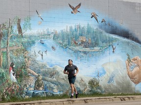 A jogger makes their way past a mural of the Edmonton river valley titled "Our Natural Home", along 100 Avenue near 168 Street, in Edmonton Monday April 19, 2021. Photo by David Bloom