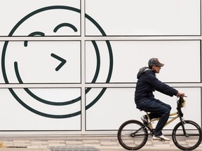 A BMX rider passes a happy face on the Feels Wellness building at 105 Street and 104 Avenue in Edmonton, on Wednesday, April 28, 2021. Photo by Ian Kucerak