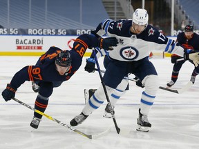 Winnipeg Jets forward Adam Lowry (17) trips up Edmonton Oilers forward Connor McDavid (97) at Rogers Place in Edmonton on Mar 20, 2021.