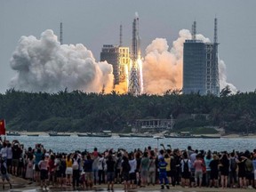 TOPSHOT - People watch a Long March 5B rocket, carrying China's Tianhe space station core module, as it lifts off from the Wenchang Space Launch Center in southern China's Hainan province on April 29, 2021. (Photo by STR / AFP) / China OUT