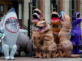An inflatable shark, triceratops, and 8 T-Rex wait to cross the street as they parade down Whyte Avenue, in Edmonton Sunday April 4, 2021. The shark is carrying an Easter basket and a sign that says, "Happy Easter from the Inflatables". Photo by David Bloom