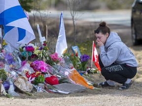 A woman pays her respects at a roadside memorial on Portapique Road in Portapique, N.S. on Friday, April 24, 2020. At least 22 people are dead after a man, who at one point wore a police uniform and drove a mock-up cruiser, went on a murder rampage in Portapique and several other Nova Scotia communities.