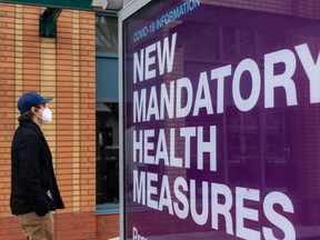 A man in a mask passes an Alberta sign announcing new mantra health measures on a bus stop near 110 Street and 82 Avenue during the COVID-19 pandemic in Edmonton, on Monday, Dec. 21, 2020. File photo.