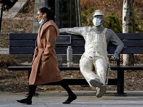 A woman walks past a statue wearing a face mask in downtown Edmonton during the COVID-19 pandemic on April 14, 2021.