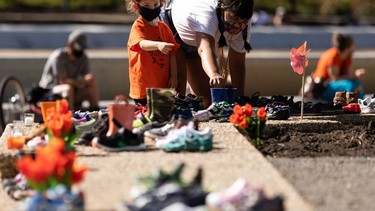 A mother and child leave a pair of children's rubber boots in memory of 215 children whose remains were found in unmarked graves at the site of the Kamloops Indian Residential School during a vigil at the "Service through Christ" statue at the Alberta Legislature in Edmonton on May 30, 2021. Photo by Ian Kucerak