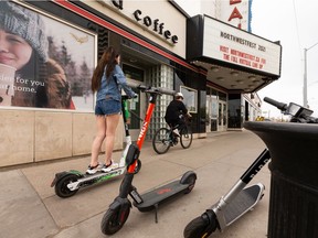 یک اسکوتر الکترونیکی و یک دوچرخه سوار در پیاده رو در امتداد خیابان 109 در خیابان 87 در ادمونتون، در روز جمعه، 14 می 2021، حرکت می کنند.