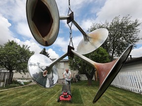 Randall (last name not given) is framed by a piece of art hanging in a tree as he mows his backyard, in Edmonton Monday June 7, 2021. Randall made the sculpture out of discarded metal stands that once held wallpaper samples. The sculpture hangs from a tree in his Rosslyn neighbourhood backyard. Photo by David Bloom