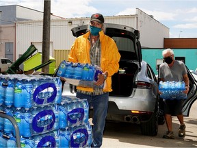 Volunteer Don Bilodeau, left, stacks a donation of bottled water from Don Kruk, right, at the Mustard Seed warehouse in Edmonton on Wednesday, June 23, 2021. With a heat wave descending upon the Edmonton region, a supply of water for those living on the street is at a dangerously low level for the non-profit organization.