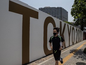 TOKYO, JAPAN - JULY 12: A man wearing a face mask runs past a Tokyo 2020 banner on July 12, 2021 in Tokyo, Japan. Japan entered its fourth state of emergency today as the government tries to contain a resurgence in coronavirus infections with less than two weeks to go before the start of the postponed Olympic Games.