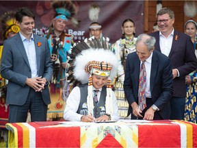Cowessess First Nation Chief Cadmus Delorme, centre, signs a document marking the transfer of control of children in care to the First Nation alongside Prime Minister Justin Trudeau and Saskatchewan Premier Scott Moe during an event held on Cowessess First Nation in Saskatchewan on July 6, 2021.