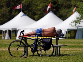 A cyclist takes an afternoon nap on a picnic table at Hawrelak Park in Edmonton on Friday July 23, 2021. The white tents in the background were set up for the Edmonton Heritage Festival which will take place in the park next weekend.