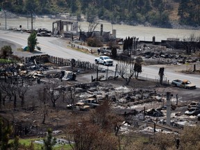An RCMP vehicle drives past the remains of vehicles and structures in Lytton, B.C., on Friday, July 9, 2021, after a wildfire destroyed most of the village on June 30.