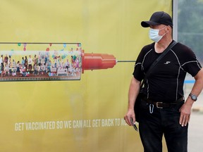 A transit passenger waits for their bus beside a COVID-19 vaccination advertisement, in Edmonton Saturday July 17, 2021.