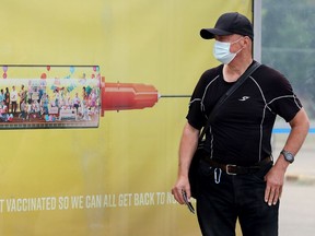 A transit passenger waits for their bus beside a COVID-19 vaccination advertisement in Edmonton on July 17, 2021.