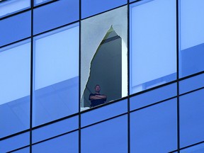 A man looks out from a broken window on the Stantec Tower in downtown Edmonton on Wednesday July 28, 2021. Police closed off the road at the base of the tower for hours while crews dealt with the issue. Larry Wong, Postmedia