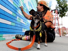 A very vocal Benito the dog guards Michelle Campos as she touches up a mural by Kenneth Lavallee on the exterior of the Ociciwan Contemporary Art Centre, 10124 96 St., in Edmonton Thursday Aug. 19, 2021.