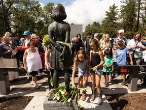 Children lay tulips at the feet of a statue of Anne Frank that was unveiled at Light Horse Park in Edmonton, on Sunday, Aug. 8, 2021. The statue was installed by the Dutch Canadian Club as part of their 75th Liberation Project. Photo by Ian Kucerak