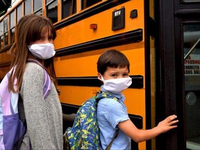 Students wearing face masks board a school bus.
