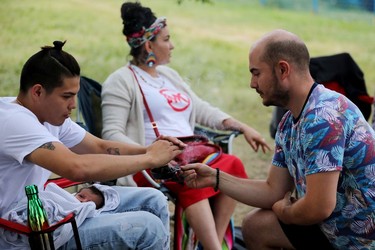 Jodell Morin holds his three week-old son Micah Mindus-Morin, as he accepts smudging from Emanuel Caparelli during a protest on the grounds of the former Charles Camsell Indian Hospital, in Edmonton Monday Aug. 9, 2021. The protesters hope to bring awareness to the discovery of over 5,000 unmarked graves at Canada's former residential school sites. Over nearly 50 days the nightly protest has hosted healers, drummers, speakers, survivors and singers. Part of the hospital site was recently searched for unmarked graves and future searches are planned.