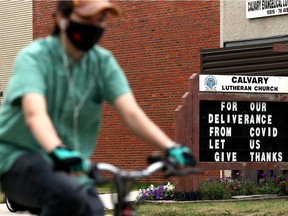 A cyclist, wearing a protective COVID-19 face mask, makes their way past a sign at Calvary Lutheran Church, 10815 76 Ave.