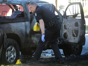 A Vancouver police officer hunts for evidence in a burned-out vehicle at Penticton and Charles following a shooting in the parkade of the Fairmont Pacific Rim hotel in Vancouver. Burning getaway cars are a hallmark of B.C. gang hits.