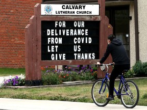 A cyclist, wearing a protective COVID-19 face mask, makes their way past a sign at Calvary Lutheran Church, 10815 76 Ave., in Edmonton on Aug. 22, 2021.
