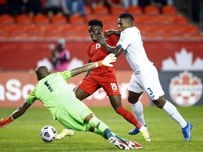 Alphonso Davies (No. 19) of Canada battles for the ball with Harold Cummings (No. 3) and goalkeeper Luis Mejia (No. 1) of Panama during a 2022 World Cup Qualifying match at BMO Field on October 13
