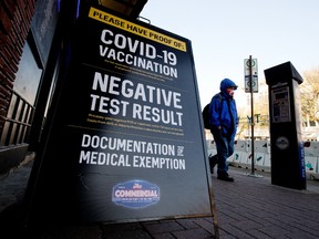 A pedestrian, wearing a face mask to protect against COVID-19, makes their way past a sign advertising the COVID-19 restrictions in place outside the Commercial Hotel-Blues On Whyte Pub on Thursday Oct. 7, 2021.
