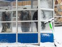 Transit riders wait for a bus on 109 Street near 107 Avenue next to a snowy Lime e-scooter in Edmonton on Nov. 16, 2021. 