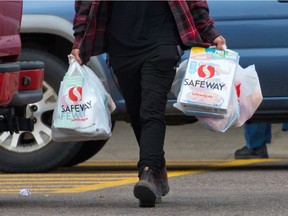 A shopper leaves a Safeway store with groceries in plastic bags. The City of Edmonton is proposing a single-use items policy to eliminate plastic shopping bags and straws as well as implement fees for reusable bags and disposable cups.