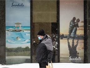 A man walks past an ad for travel to sunny destinations on Vision Travel's window on 108 Street in Edmonton, on Tuesday, Nov. 16, 2021. The Capital region has been hit by the first major snowstorm of the season.