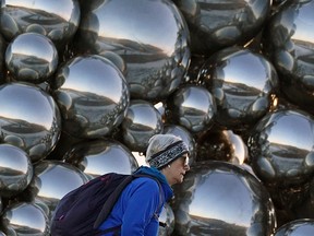 A woman walks past the Talus Dome art installation near the Quesnell Bridge on Whitemud Drive on Nov. 29, 2021. Composed of nearly 1,000 handcrafted stainless steel spheres, the piece of public art forms an abstract talus shape, reflecting the sky, weather and the river as motor vehicles that pass by.