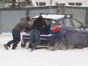 Good samaritans push a motorist stuck in the 38 Avenue and 38 Street intersection, in Edmonton Tuesday Nov. 16, 2021. A City of Edmonton phase 1 parking ban will begin at 7 p.m. and remain in effect until the city has cleared major roadways such as arterial and collector roads as well as freeways, bus routes and roads with "Seasonal No Parking" signs.