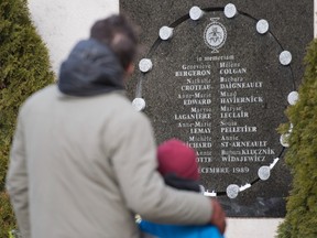 A man and child stand in front of the commemorative plaque on the wall of Polytechnique in Montreal, Sunday, Dec. 6, 2020, on the 31st anniversary of the murder of 14 women in an anti-feminist attack at Ecole Polytechnique on December 6, 1989. The COVID-19 pandemic continues in Canada and around the world. THE CANADIAN PRESS/Graham Hughes