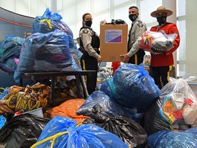 The RCMP organized the collection of everyday items, as Cpl. Kandis Hiscock, Cpl. Mohamad Khaled and in red serge dress, Sgt. Ron Bumbry of the Alberta RCMP Community Engagement Unit, hold up some of the donated items for Afghan families arriving in Alberta, at the RCMP K Division in Edmonton, Thursday, Dec. 16, 2021.