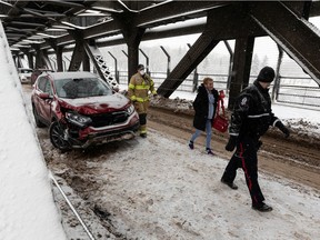 An Edmonton Police Service officer and a Edmonton Fire Rescue Service firefighter are seen helping a driver after they were involved in a two-vehicle crash on the High Level Bridge during a snowstorm in Edmonton on Wednesday, Dec. 22, 2021.